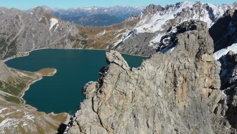 Aerial-shot-of-a-man-hiking-and-climbing-up-the-last-steps-to-reach-the-top-of-a-cliff-to-see-the-beautiful-view-of-the-valley-and-mountains-in-front-of-him-in-Lunersee,-Switzerland-during-summer