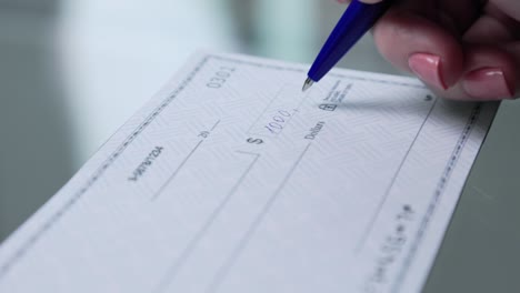 business woman hand signs and filling bank check for one thousand 1000 dollars