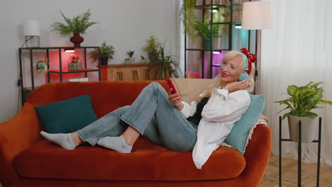 feliz mujer relajada con auriculares inalámbricos bailando escuchando música rock n roll favorita en el sofá de casa