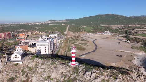 Lighthouse-surrounded-by-mountainous-terrain-along-coast-and-resorts-in-Cabo