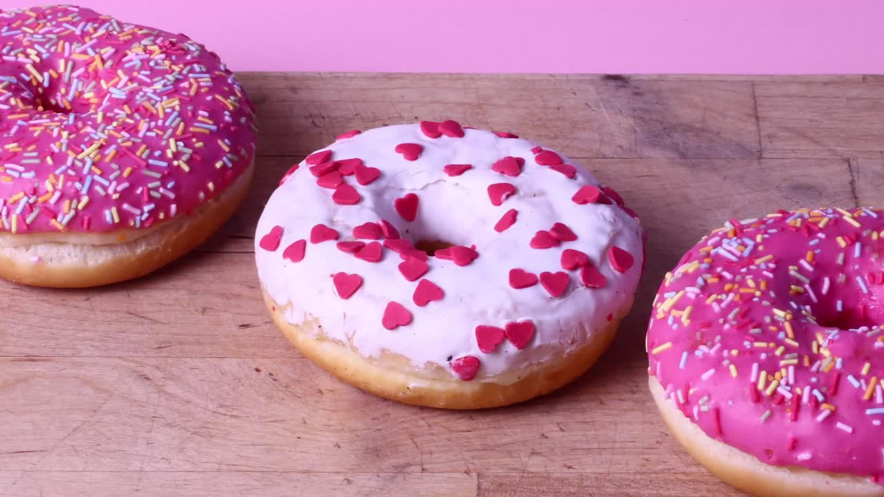 Tasty rotating pink donuts. Stop motion on pink background. Pink glazed donut with sprinkles, time-lapse on pink background. Lower angle view.