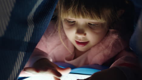 cute-little-girl-using-digital-tablet-computer-under-blanket-enjoying-learning-on-touchscreen-technology-playing-games-having-fun-at-bedtime