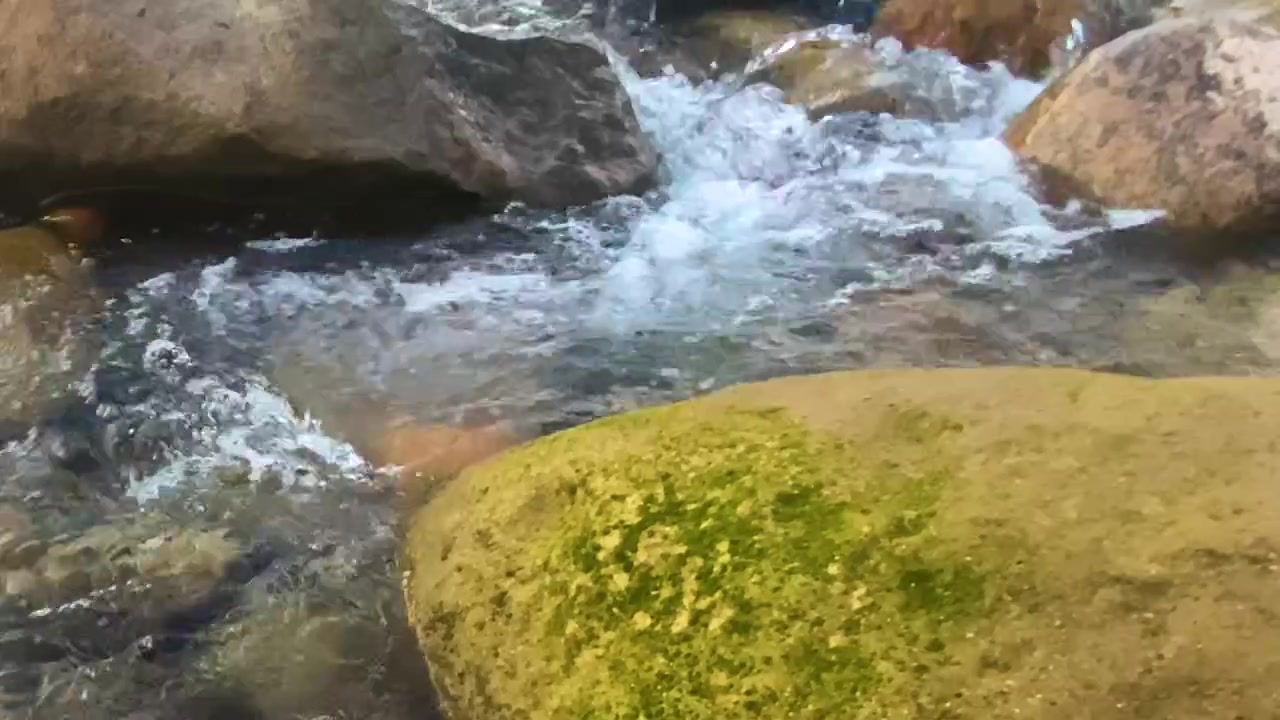 Tranquil stream flowing through large rocks and boulders with green algae
