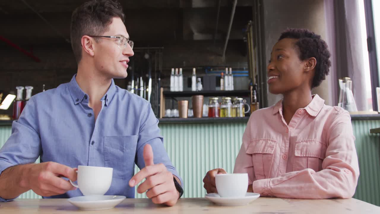Two diverse male and female friends sitting at table in cafe drinking coffee and talking