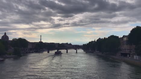 a stunning slow motion captures the beauty of france's seine river as a boat gliding along the waters and flows gently through paris, with trees on both banks it, and gray cloudy and blue sky