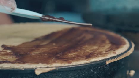 spreading chocolate cream over frying pancake on crepe maker