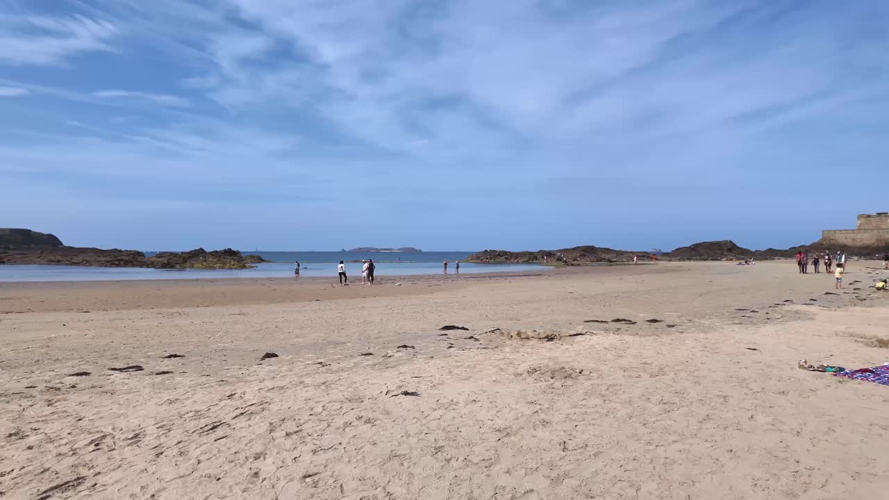 Sunny sandy beach around fortified old town of Saint Malo and distant Fort National, Brittany, France