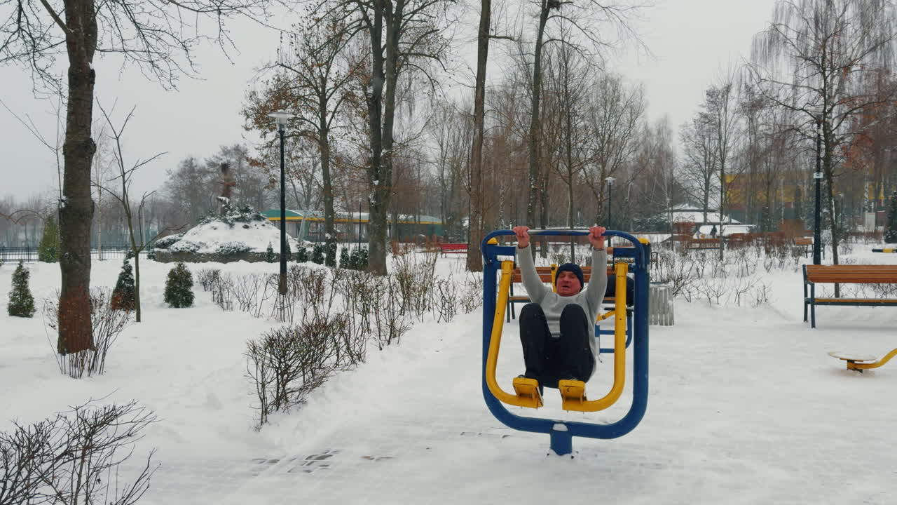 Doing sport in winter outdoors in the park. Fit senior man exercising on simulator on snowy day.