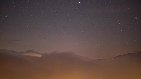 Timelapse-De-Estrellas-En-Movimiento-En-La-Noche-Por-Encima-De-Las-Nubes-Con-Montañas-En-Segundo-Plano.