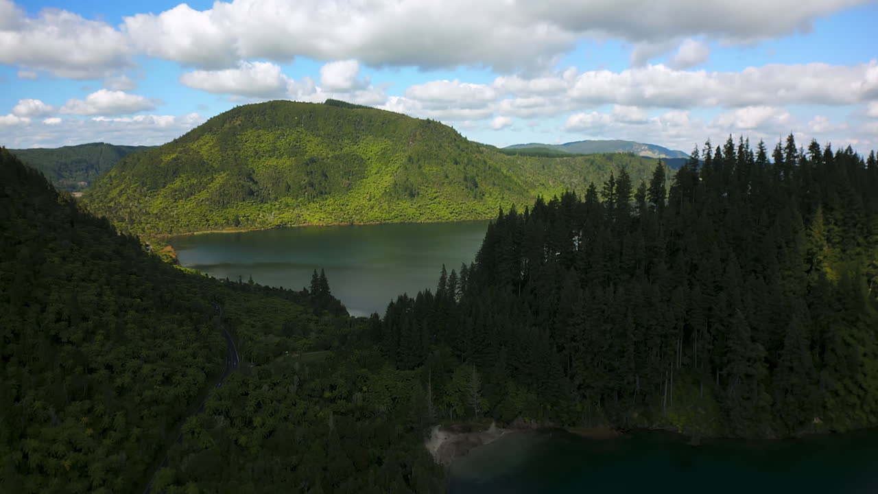 Lush forested hills and calm blue lake under a partly cloudy sky in Rotorua New Zealand