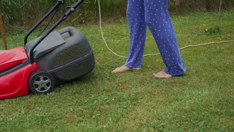 barefoot young girl mowing grass with a lawn mower in garden. bare female feet walking behind lawn mower in back yard