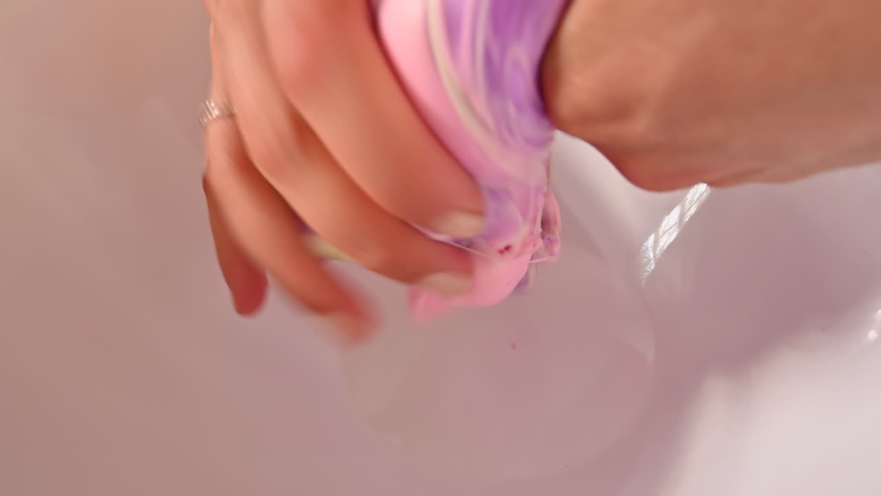 Donna che mescola slime rosa con slime verde e viola su sfondo bianco