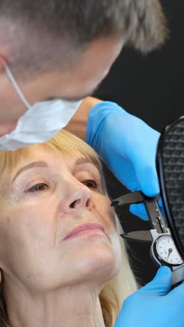 a woman undergoes ear measurement by a dentist, who checks her facial features like nose, mouth, eyes, and gestures to ensure accuracy.