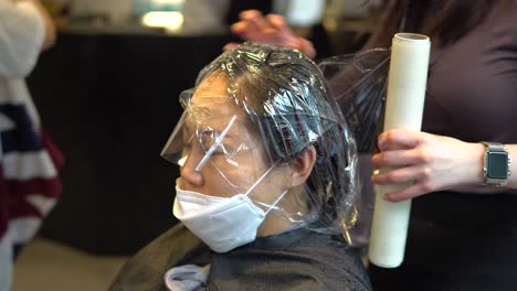 hairdresser put on plastic wrap on asian woman hair at the beauty salon during a covid-19 pandemic