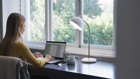 Biracial-woman-sitting-at-desk-using-smartphone-and-laptop-at-home,-slow-motion,-copy-space