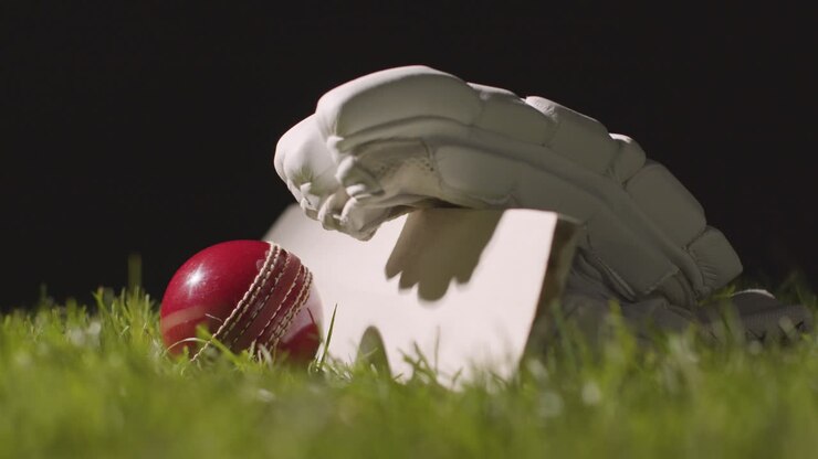 Natura morta di cricket con primo piano di mazza, palla e guanti adagiati sull'erba 5