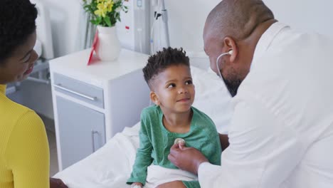 Médico-Varón-Afroamericano-Examinando-A-Un-Paciente-Infantil,-Usando-Estetoscopio-En-El-Hospital