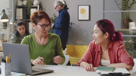 Senior-Female-Manager-and-Young-Trainee-Using-Laptop-and-Talking