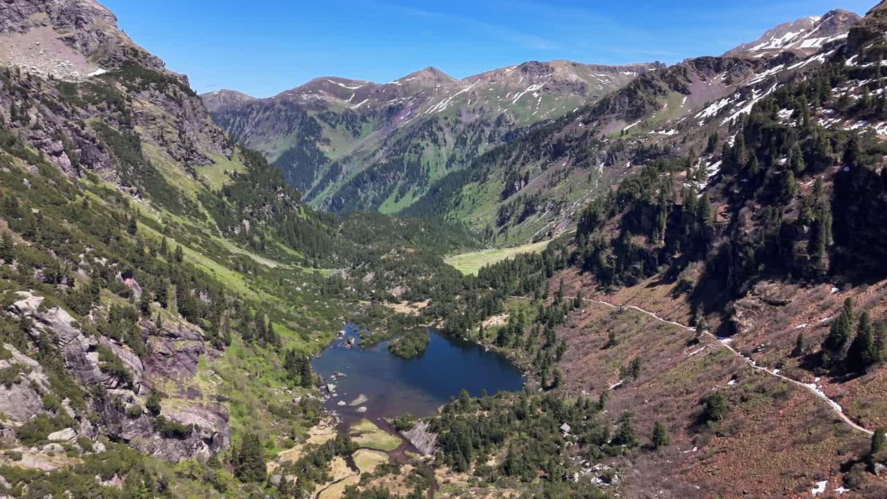 Murgsee valley showing a serene alpine lake surrounded by towering mountains, dense forests, and a clear blue sky, capturing the unspoiled essence of nature, Switzerland, drone establishing shot
