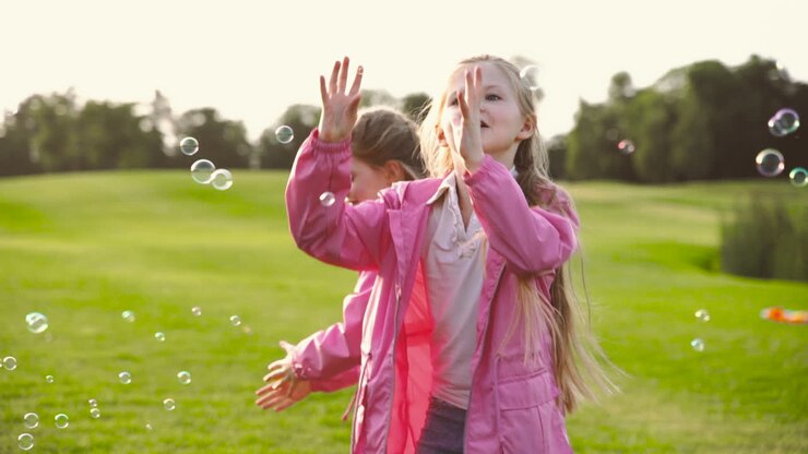 Sorelline felici con vestiti identici che acchiappano bolle di sapone nel parco
