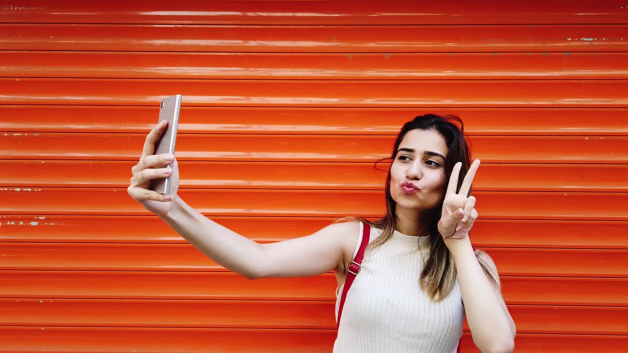 Beautiful young girl takes selfie with smartphone in front of orange,red background