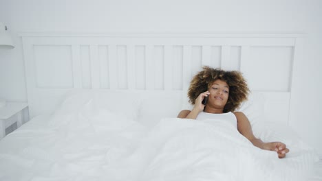 mujer sonriente en la cama con una llamada telefónica