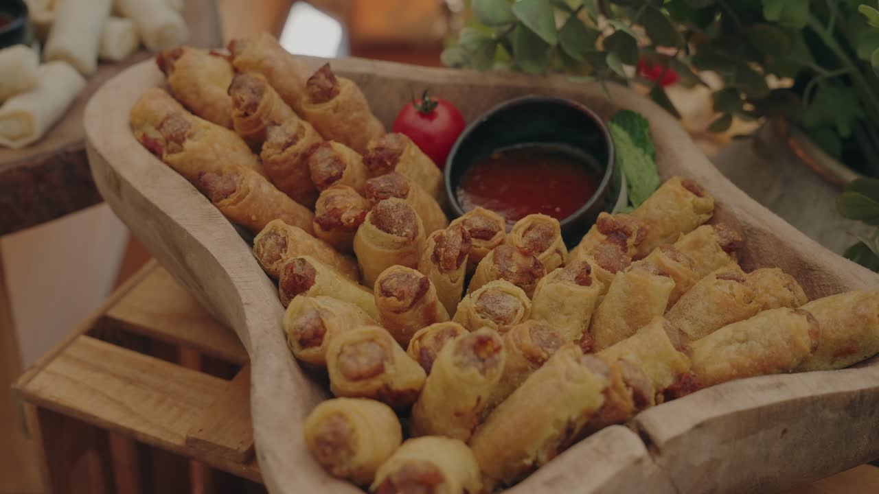 In tavola, involtini di salsiccia dorati disposti in una ciotola di legno con salsa di pomodoro e erbe aromatiche