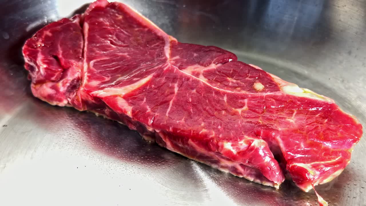 A juicy, large steak sizzling in the pan. Close-up shot