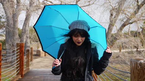 una mujer bonita que se ve linda y sonriente con un paraguas azul durante un descanso en la tormenta de lluvia en cámara lenta