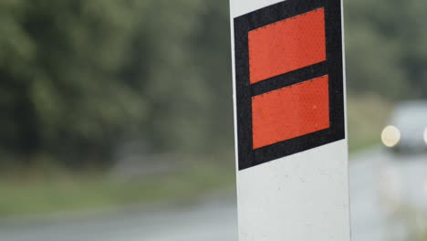 orange caution reflector sign in rain as cars pass background, close-up