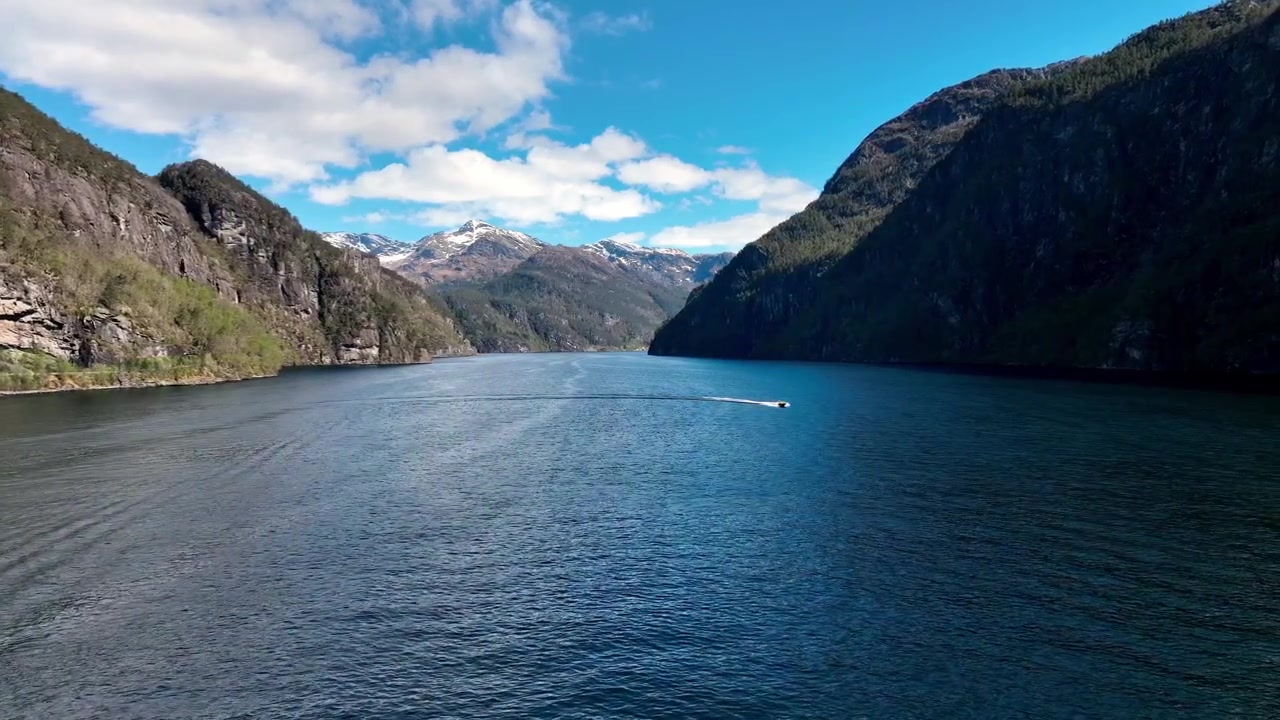 RIB-Touristenboot wendet tief in einem norwegischen Fjord an einem sonnigen Frühlingstag mit schneebedeckten Gipfeln