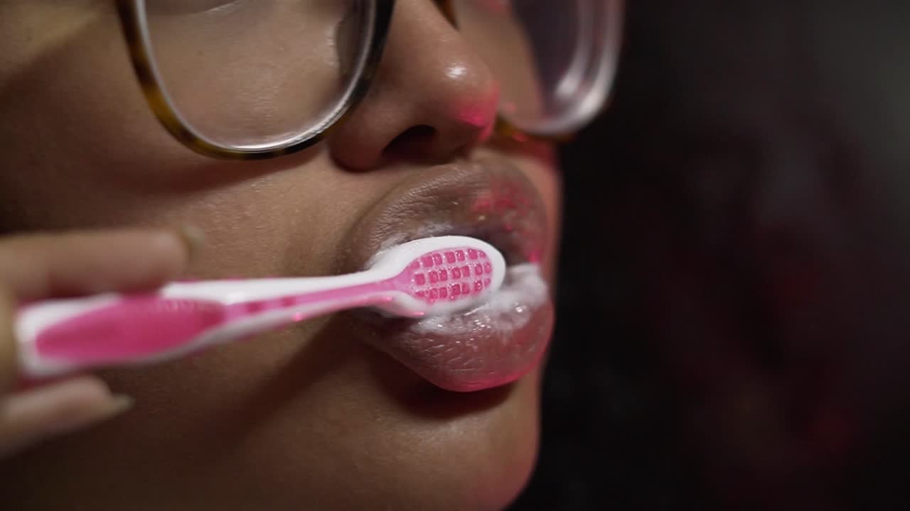 mujer negra cepillándose los dientes con un cepillo rosa en el baño