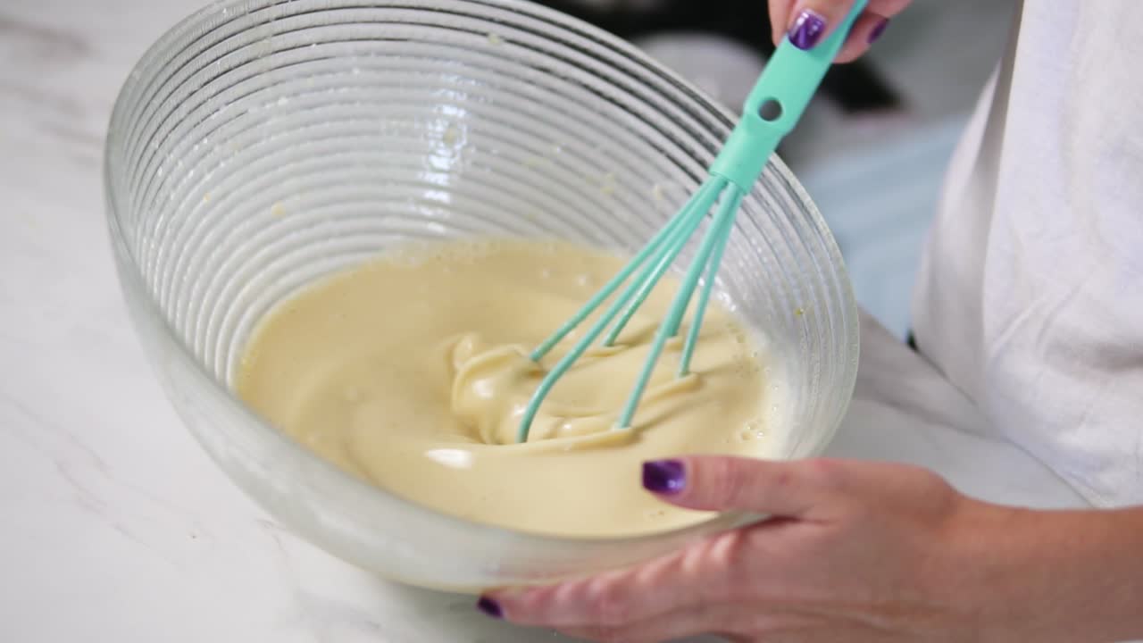 Close Up view of woman's hands mixing ingredients to prepare dough in the the bowl using whisk. Home cooking. Slow Motion shot