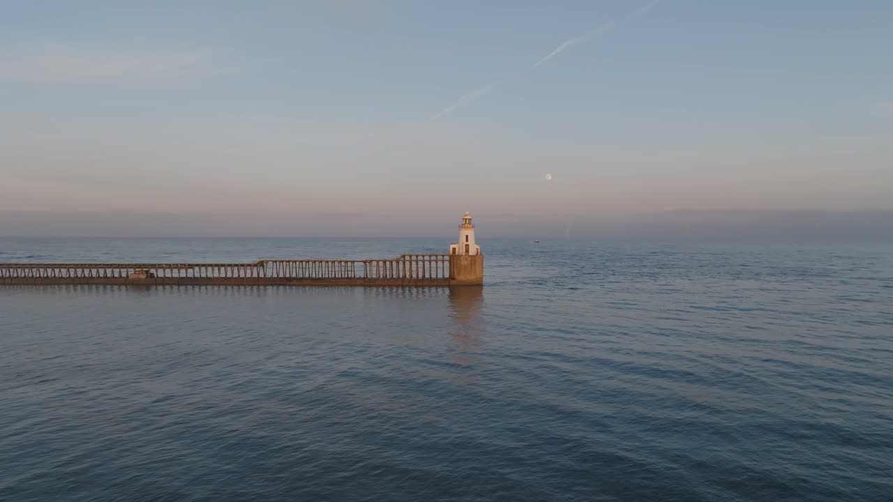 The iconic lighthouse framed by a peaceful twilight sky and the rising full moon.