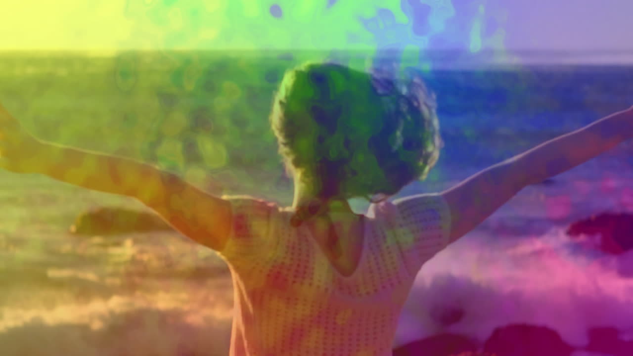 Person with arms outstretched over colorful abstract animation by ocean