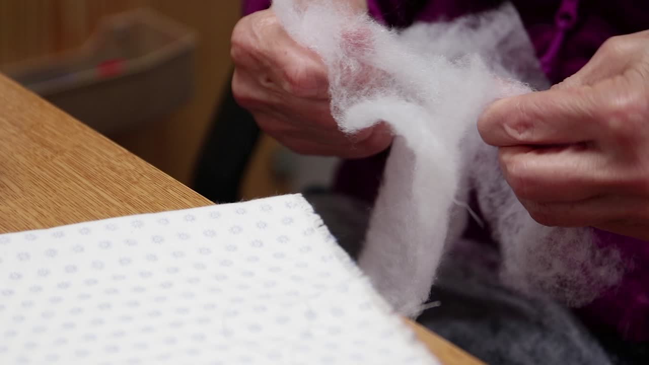 Elderly seamstress selecting filter padding for handmade production of covid virus mask