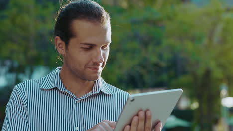 young man smiling while using a tablet outdoors