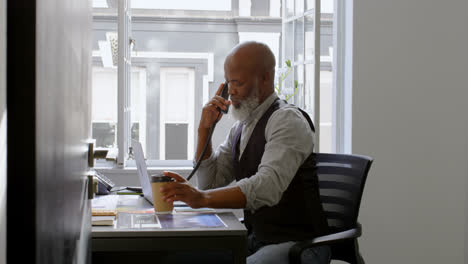 businessman having coffee while talking on landline and using laptop at desk 4k