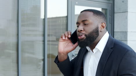 afro businessman arguing on smartphone in city. male executive talking on phone
