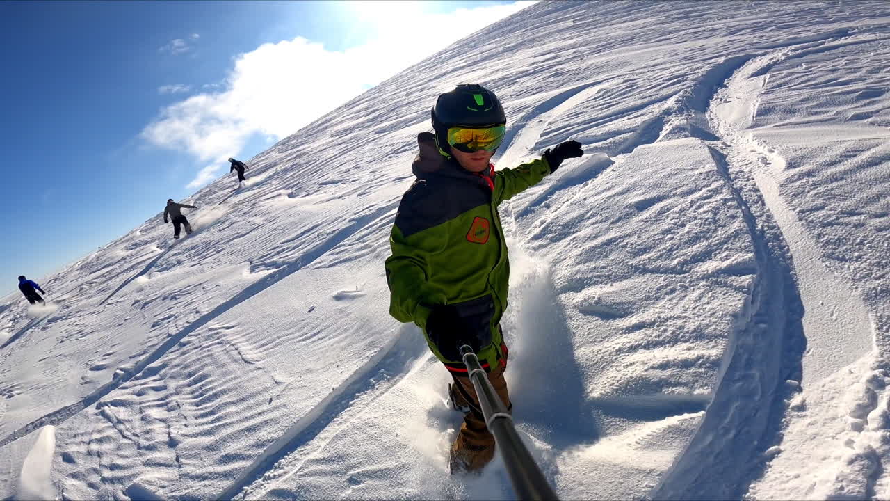 Sportsman rides on the snowboard taking selfie. Practicing active kind of sport in the mountains.