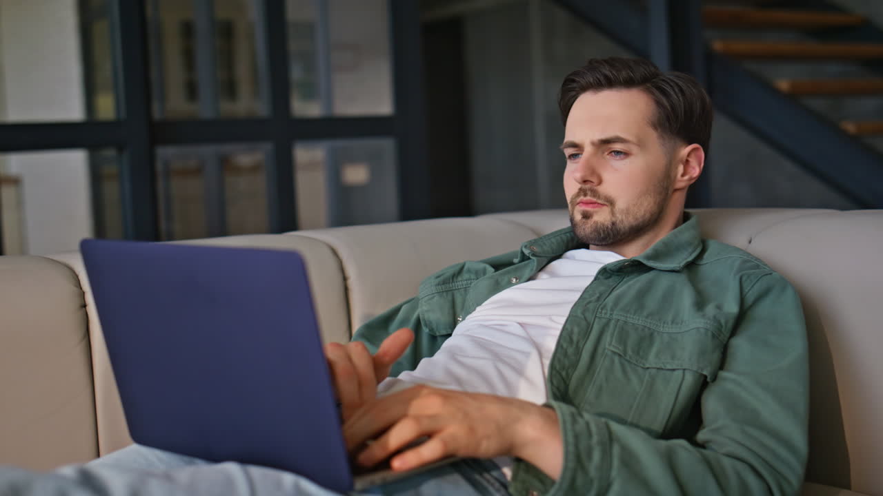 Home guy typing laptop working in sofa closeup. Relaxed man browsing web resting