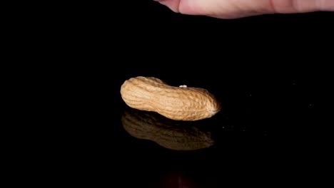 robust peanut is smashed with a fist on a reflective black surface - slow motion