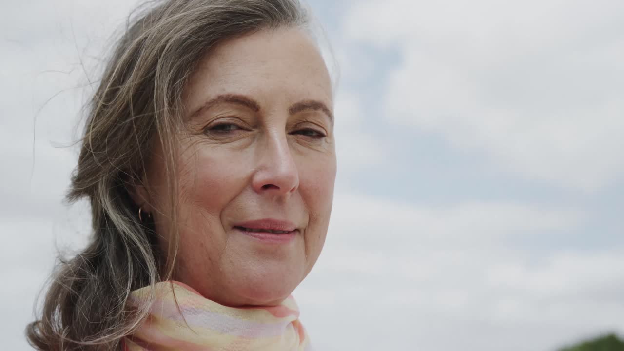 retrato de una feliz mujer caucásica mayor sonriendo contra el cielo nublado, en cámara lenta
