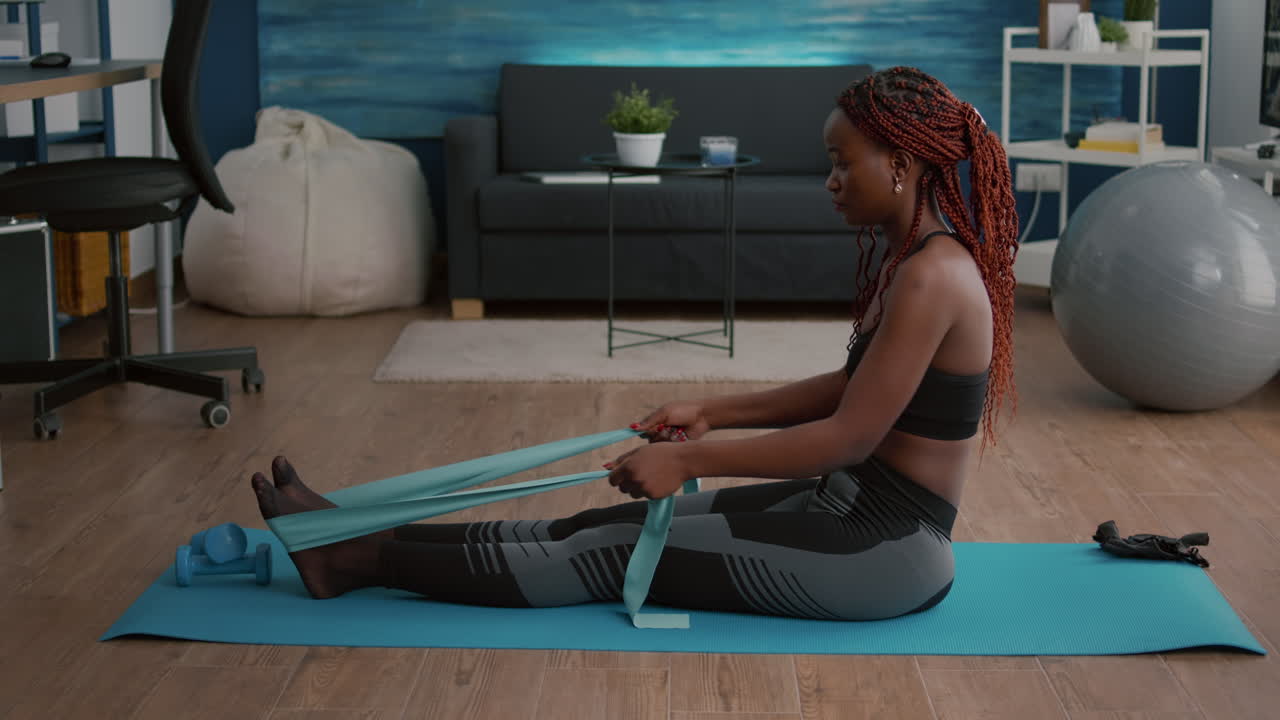Slim woman with black skin in sportswear exercising body muscle using fitness bands