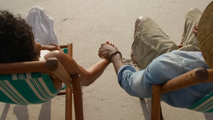Inquadratura dall'alto di una coppia afroamericana che si rilassa mano nella mano su una sdraio in spiaggia