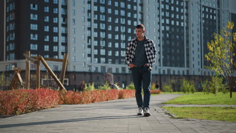 young white boy strolls on paved sidewalk with hands in pockets during sunny day as others move in blur background near modern high-rise buildings and landscaped greenery in quiet residential area