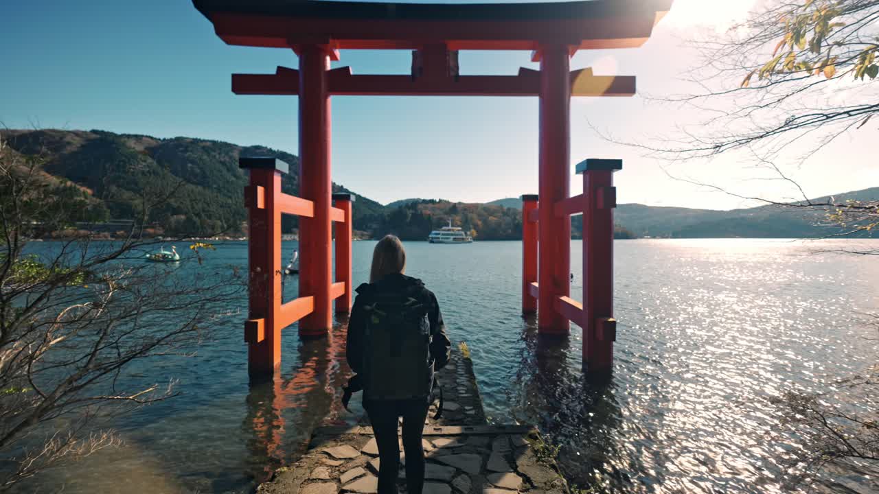 un videoclip cinematográfico de una mujer caminando con gracia a través del santuario de hakone, en el pintoresco telón de fondo del lago ashi.