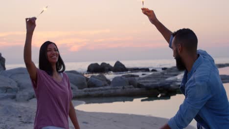 feliz pareja joven de raza mixta divirtiéndose con chispas en la playa 4k