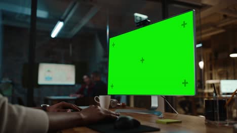 primer plano de un gerente de proyecto afroamericano negro haciendo una llamada de video en una computadora de escritorio con pantalla verde en una oficina creativa ocupada.