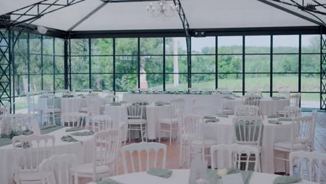 elegant wedding reception setup with white tables and chairs in glass-walled venue